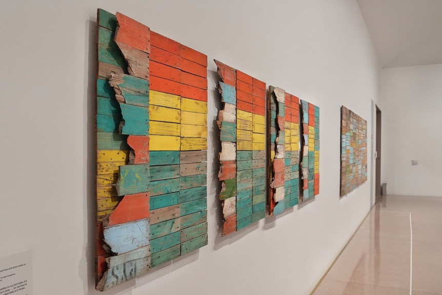 Three colourful artworks that include different planks of woods in yellow, orange, turquoise, light blue and white in gallery