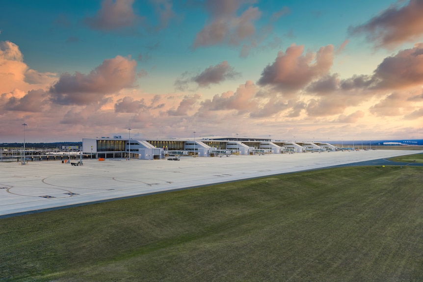 A wide shot of a brand new airport terminal from the outside and its runway on a sunrise morning.