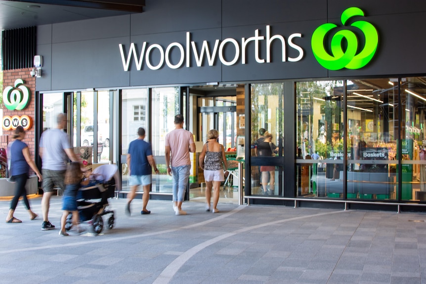The outside of a Woolworths supermarket. People walk in the entrance.