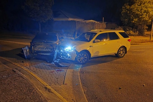 Two cars that have clearly been in collision with one another are picture at an intersection at night.