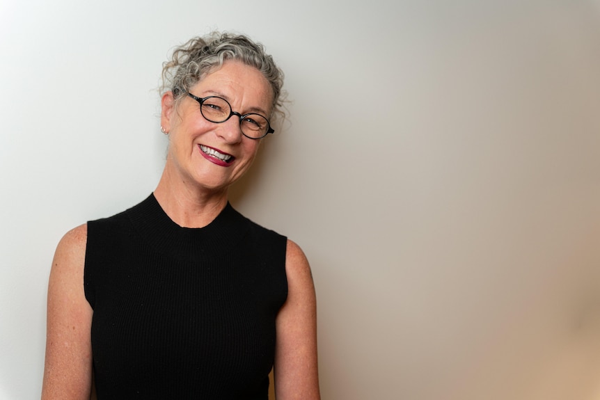 A woman with grey hair tied back and black rimmed glasses smiling at camera.