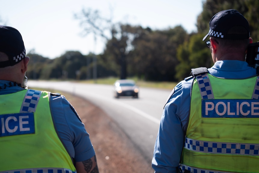 Two police look at a car coming down the road