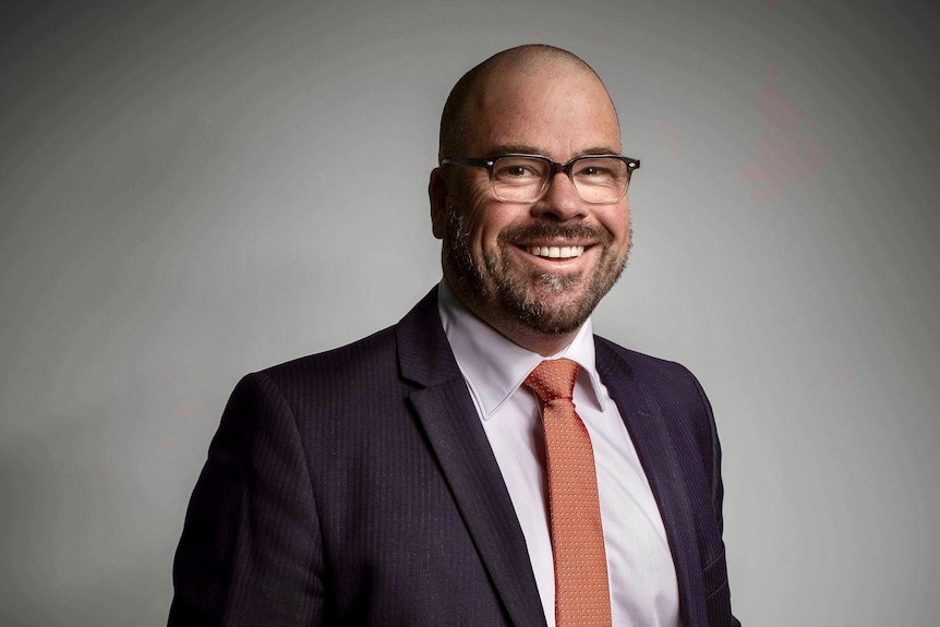 A man in a suit stands inside and smiles at the camera