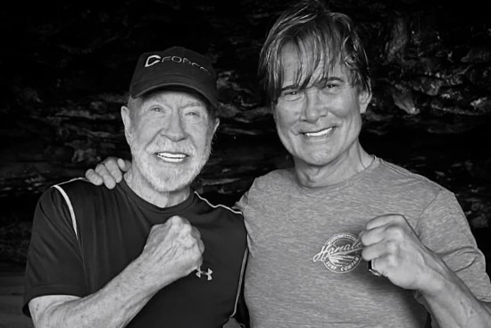 Black and white image of two men with their arms around each others' shoulders holding a fist up to the camera