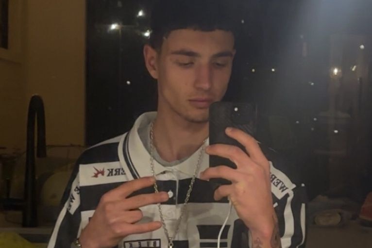 Young man with short dark hair and wearing a black and white top looking at mobile phone.