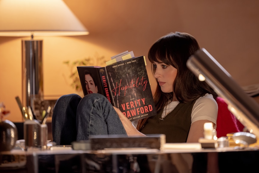 A woman sitting at a desk enthralled in a novel written by Verity Crawford