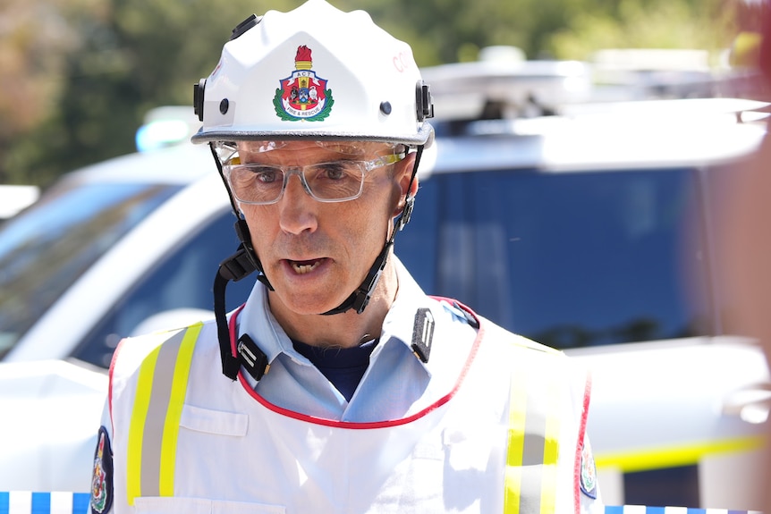 A man in a white helment speaks to reporters.
