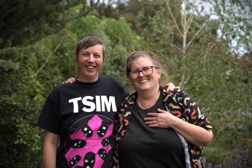 Two women put their arms around each other and smile at the camera.