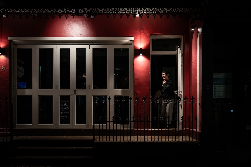 Lights glow on the red exterior of a building with woman closing white doors