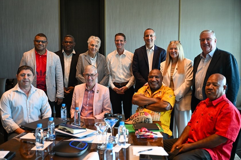 A group of male and female leaders sit at a table and some standing behind, posing for a photo.