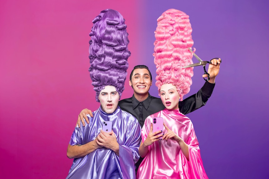 Eddie Perfect, 48, and Karis Oka, 28, shocked, in purple and pink wigs, faces painted white, Noah Szto holding scissors above.