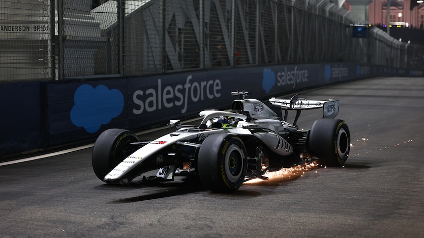 An F1 driver steers his damaged car back to the garage as sparks fly under the vehicle.