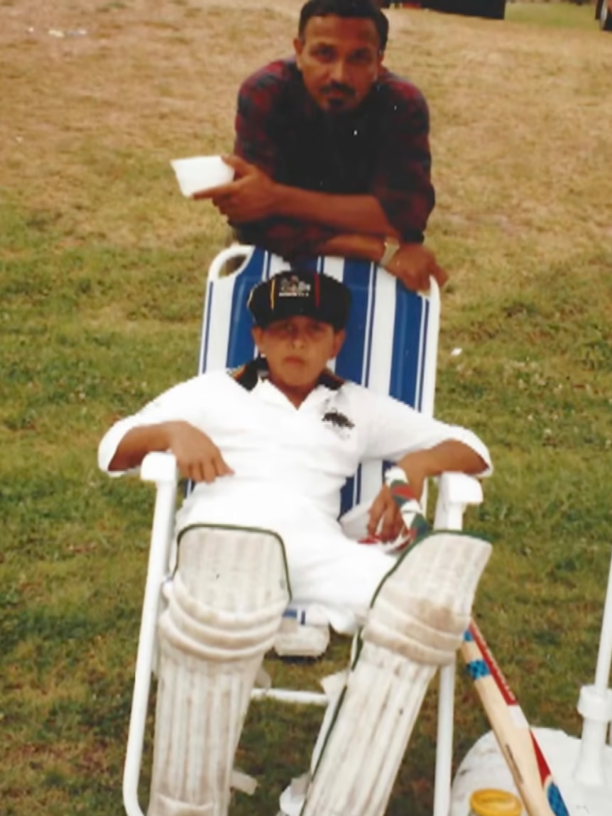 Usman and Tariq Khawaja on the grass. Usman is seated and wears cricket whites while Tariq leans over the top.