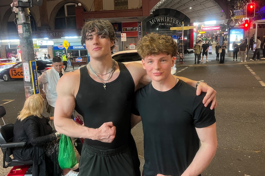 A muscled man in a black singlet top puts his arm around a teenager in a black tshirt