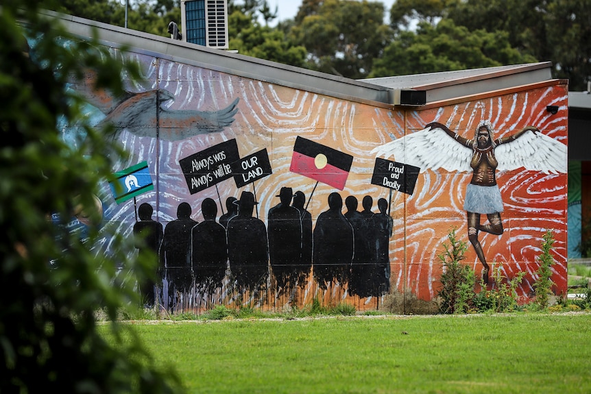 A colourful wall mural depicts Indigenous pride in the grounds of an outdoor space