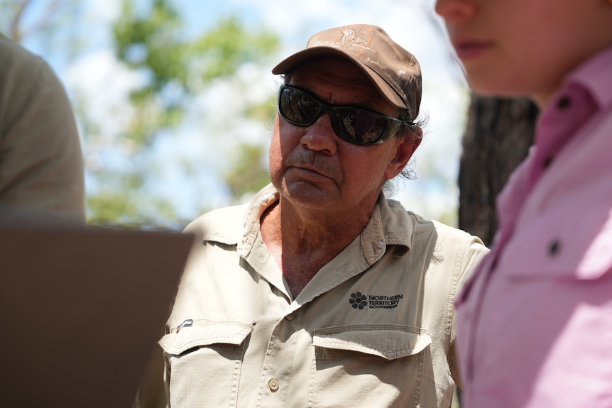 Uniformed ranger, Darius Nasir, wears cap and sunglasses as he looks over Ryan Sauermann's shoulder to see the laptop he holds.