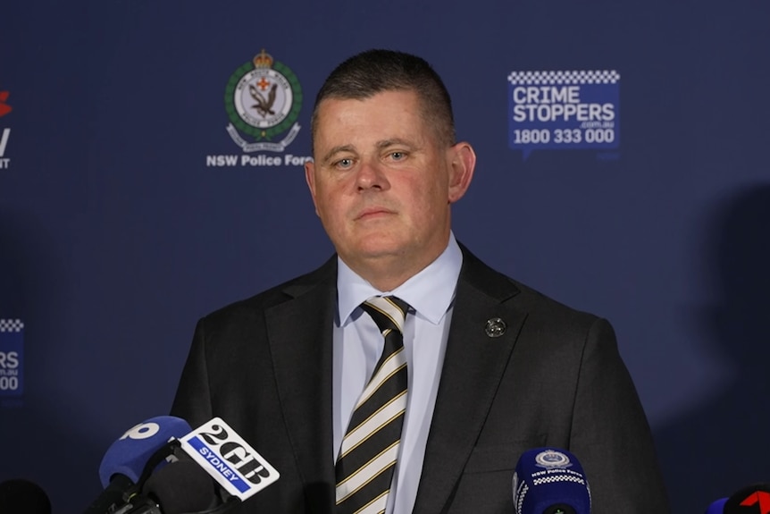 Acting Superintendent Smith looking straight ahead, wearing a suit and striped tie, at a police press conference.