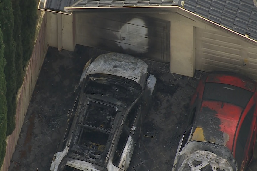 An aerial shot of two burnt out cars in a driveway with damage to a garage door.
