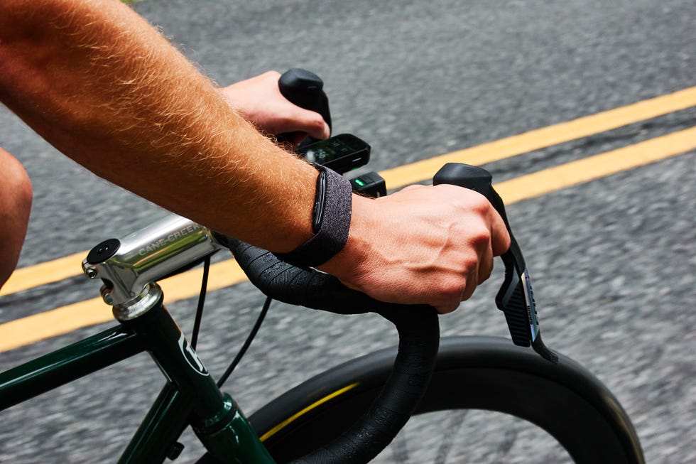 Close-up of hands gripping bicycle handlebars with a smartwatch on the wrist, on a paved road with yellow lines. Close-up of hands gripping bicycle handlebars with a smartwatch on the wrist, on a paved road with yellow lines.