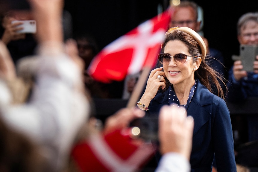 Denmark's queen mary smiles at a crowd as Danish flags fly nearby