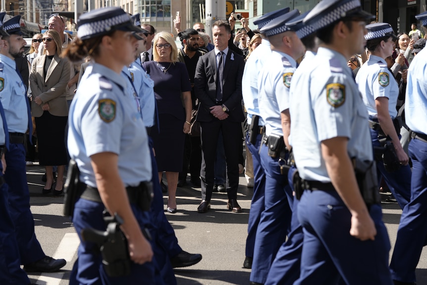 Chris Minns looks on as police officers walk by.