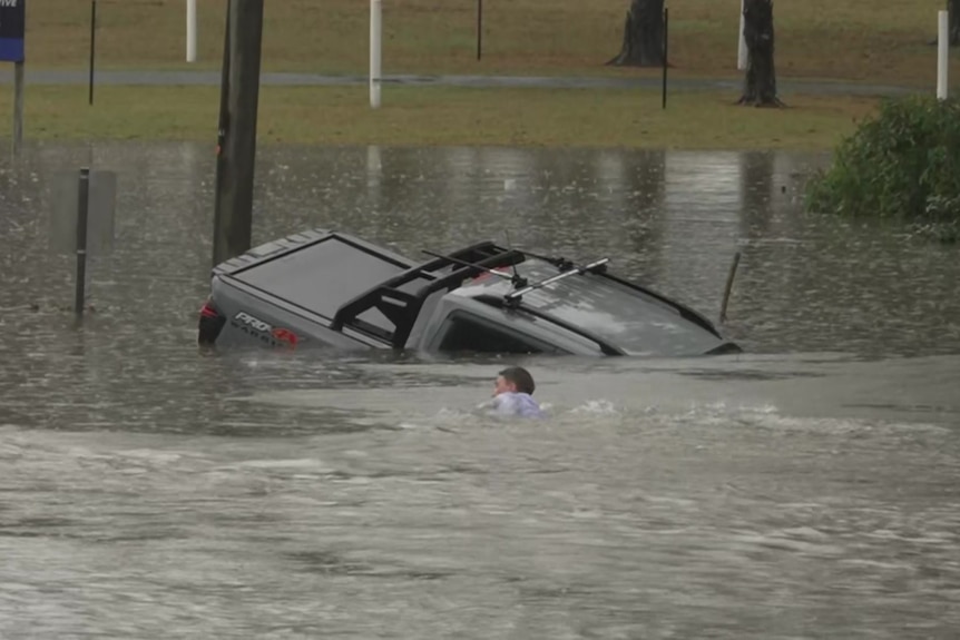 ABC reporter Will Murray swimming to a sinking car in floodwaters.
