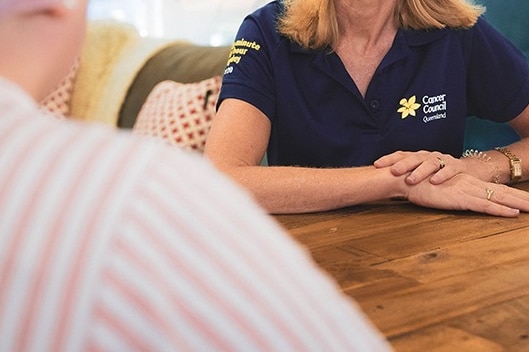 A woman wearing a blue Cancer Council polo sitting at a table with another person.
