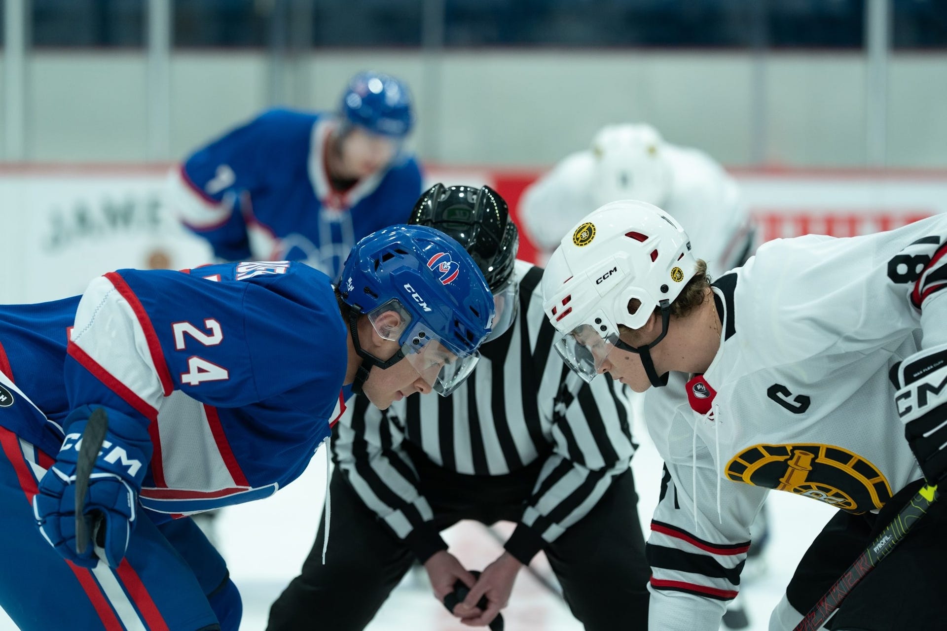Two hockey players face off at center ice with a referee observing in the background. Two hockey players face off at center ice with a referee observing in the background.