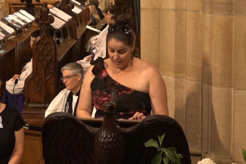 Woman with brown hair and black and red dress speaks at church lectern
