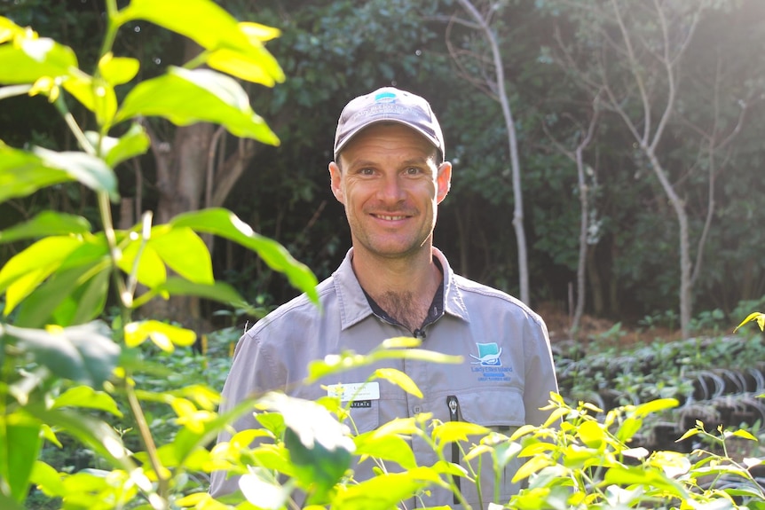 A smiling man wears a baseball cap while standing outside on a sunny day.