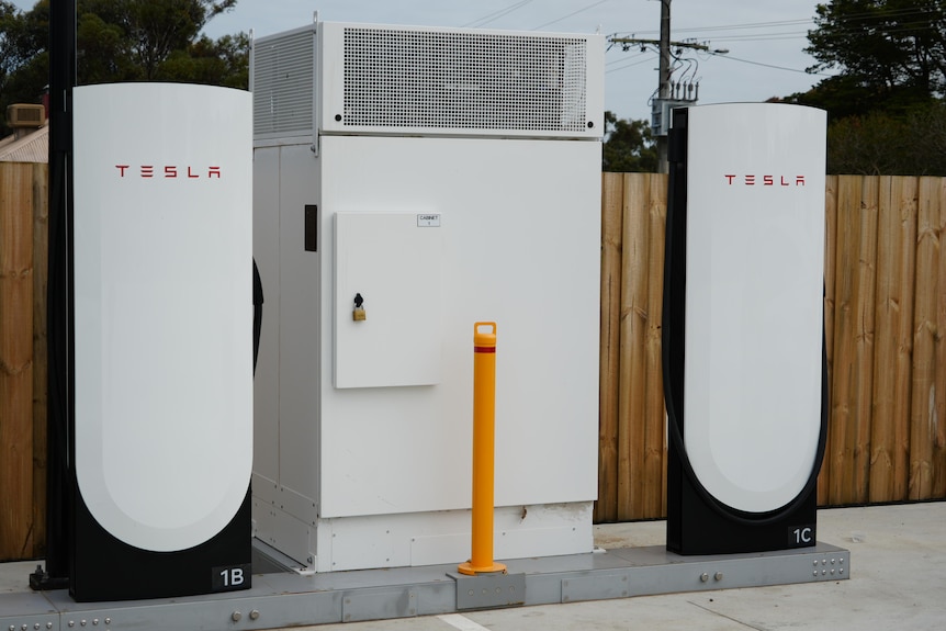 A large metal box stands between two Tesla Supercharger stations.
