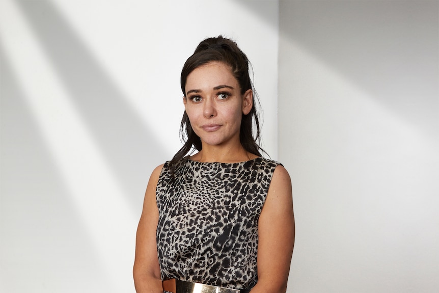 Azita Arian wears a leopard print sleeveless top and stands in a room with white walls with a serious expression on her face.
