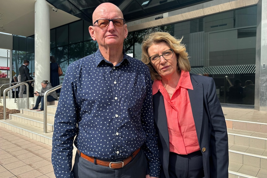 couple posing for camera showing a bald man and a woman in suit