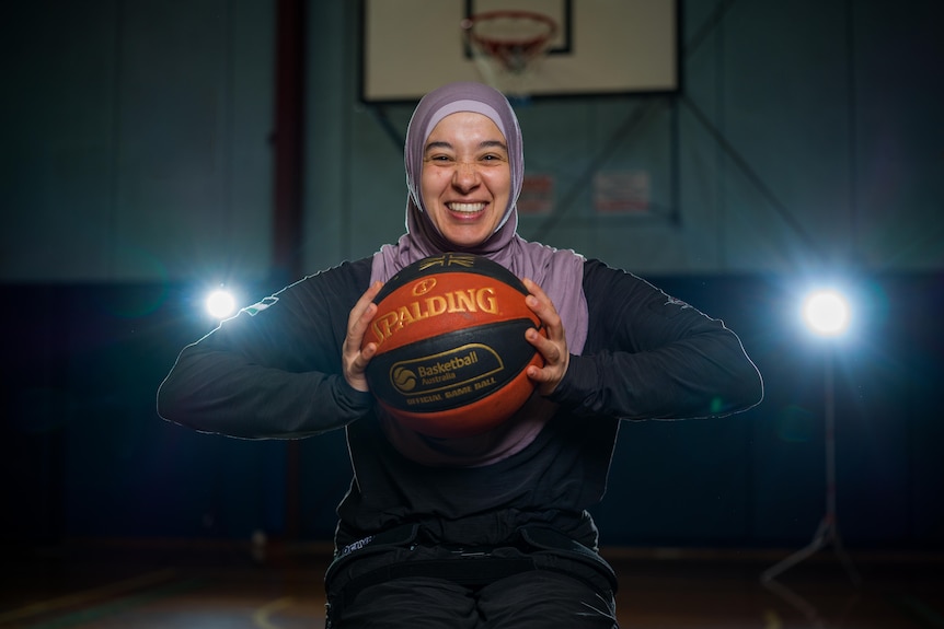 Reema El Qassem, grinning fiercely, holds a basketball in front of her.