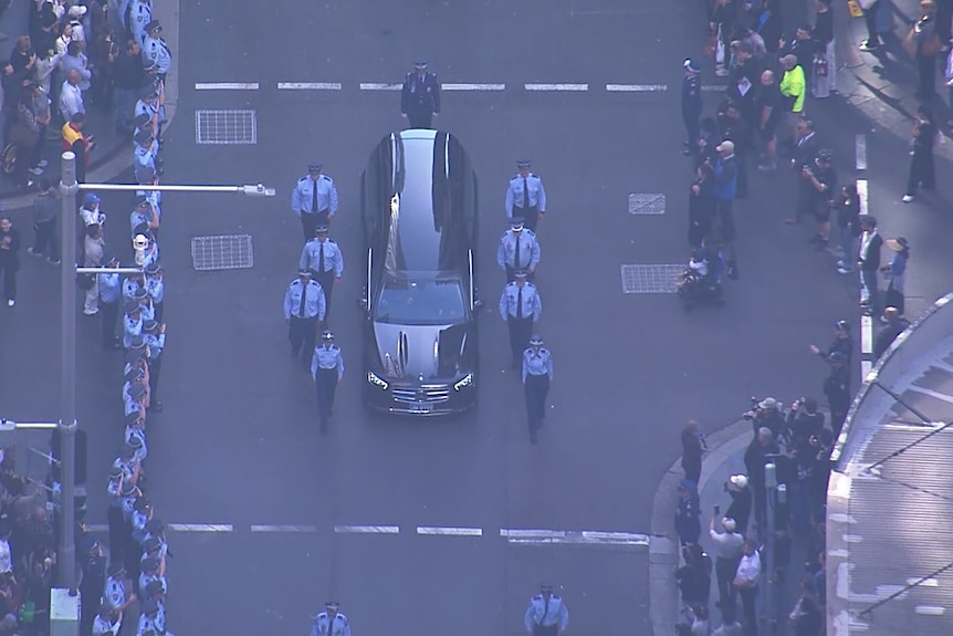 An aerial image showing police officers walking alongside a funeral hearse.