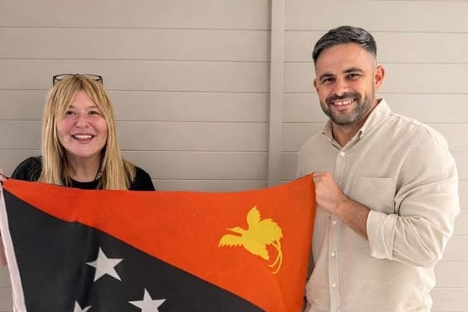 A man and woman hold a red, black, white and yellow PNG flag.