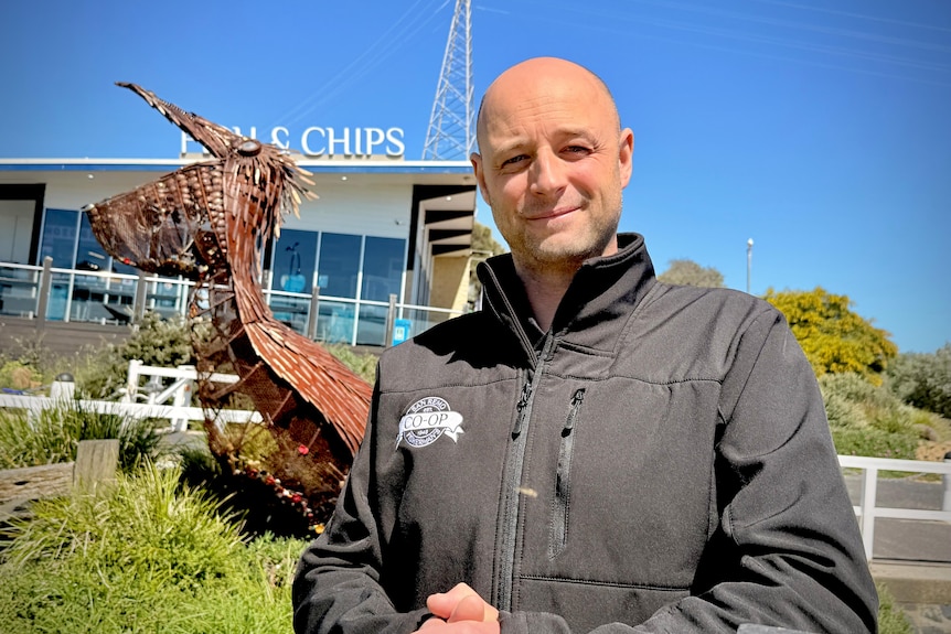 Image of a man in a black jacket standing in front of a fish and chip shop.