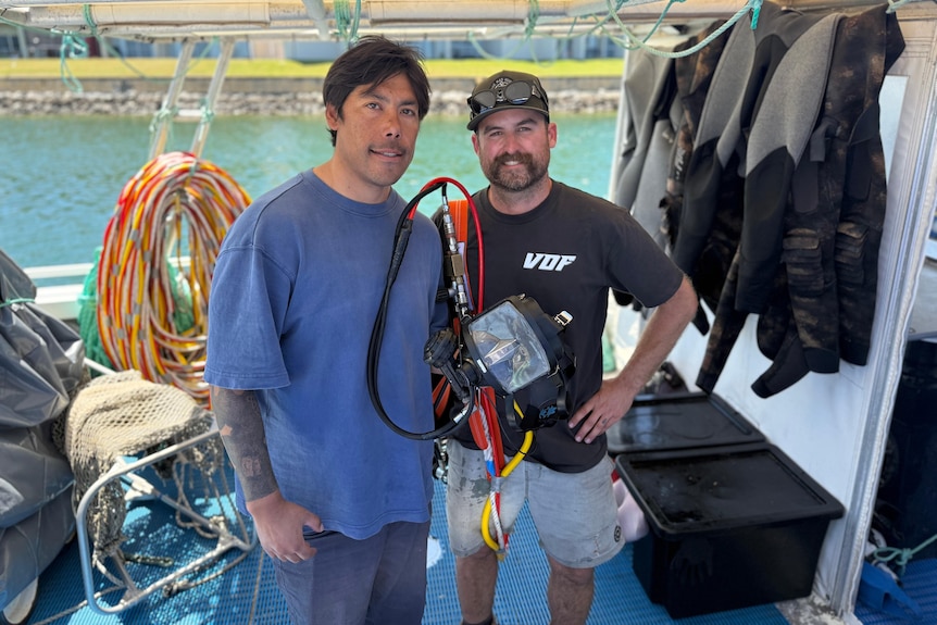 Two dark-haired men, one with a handlebar moustache, standing on a fishing boat.