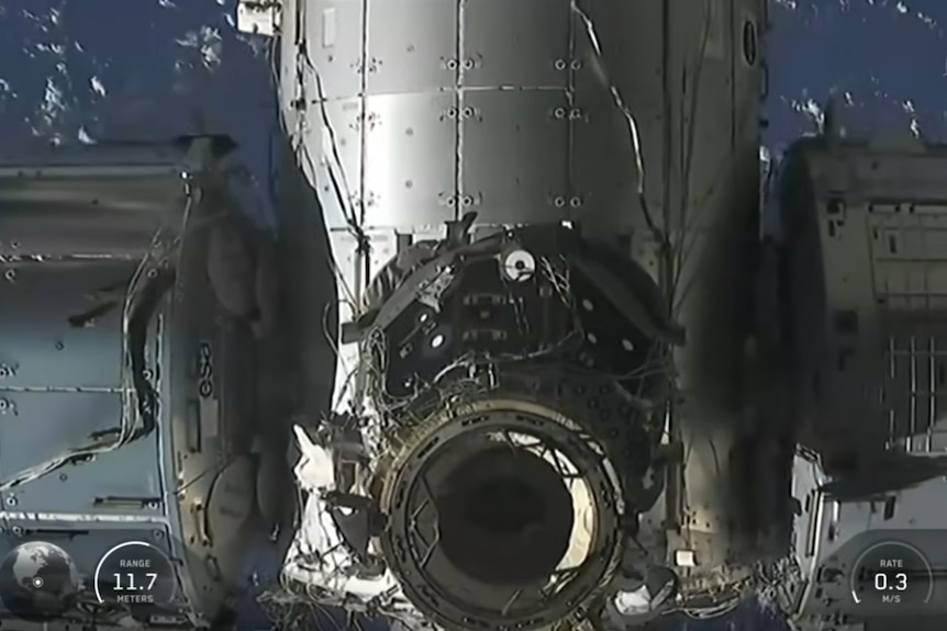 The metallic grey exterior of the International Space Station, with a large circle opening in the centre and two adjacent wings.