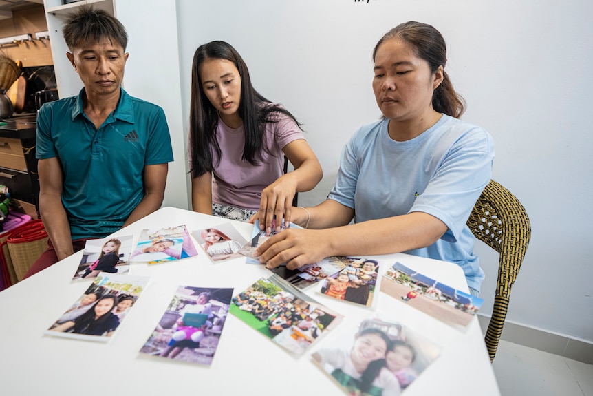 A man and two women, all with dark hair, sit at a table looking at family photos.