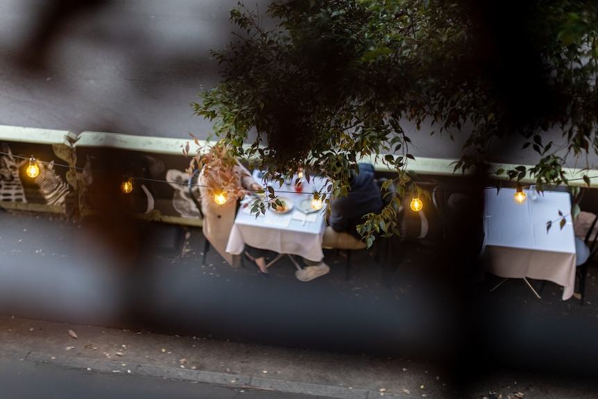 view from above looking at three tables with white tableclothes through trees only one with diners