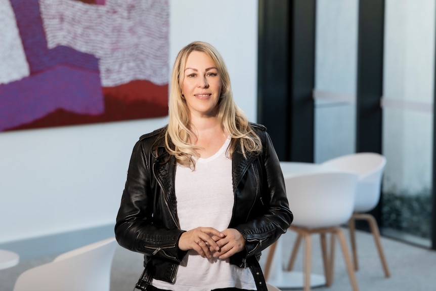 A blonde-haried woman in a black leather jacket and white t-shirt.