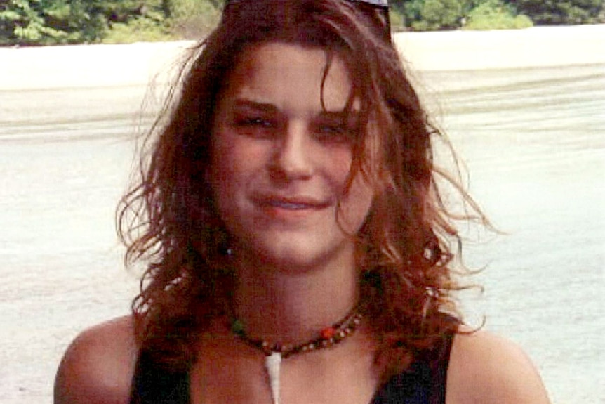 A girl looking at the camera with a beach behind.