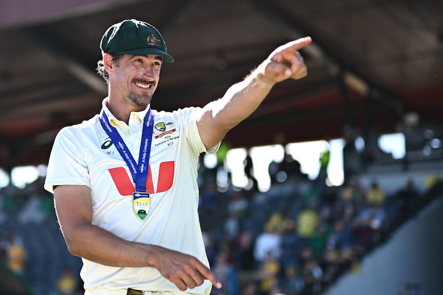 Mitchell Starc points with his left hand while wearing medal