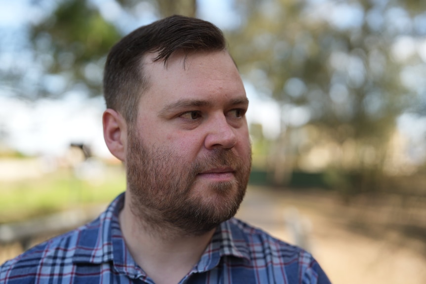 Chris has a short dark beard and hair, and looks to his left.