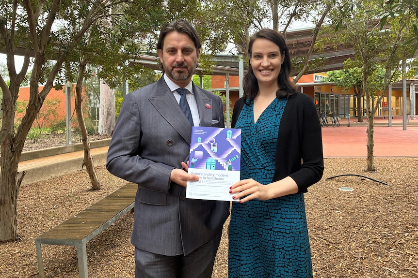 A man in a suit and a woman in a blue dress holding a printed booklet.