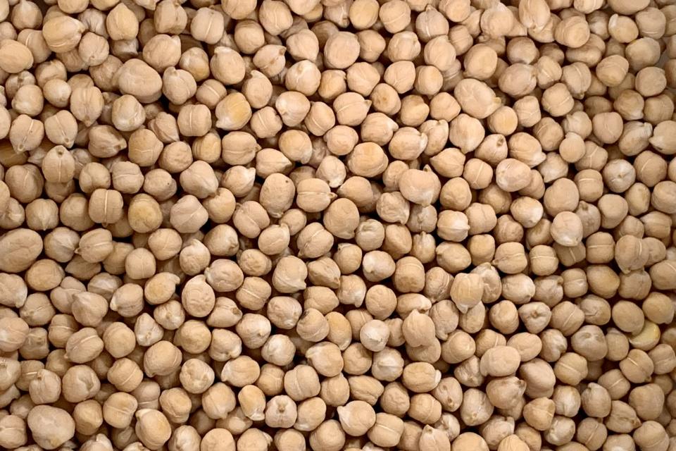 Close-up view of a large quantity of dried chickpeas filling the entire frame. The round, beige legumes vary slightly in size and colour, creating a textured pattern with no other objects visible.
