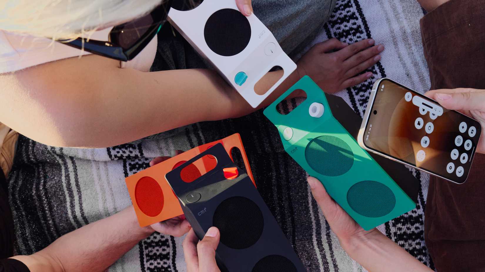 Top-down view of people outdoors holding four colorful CMF speakers and a Nothing smartphone