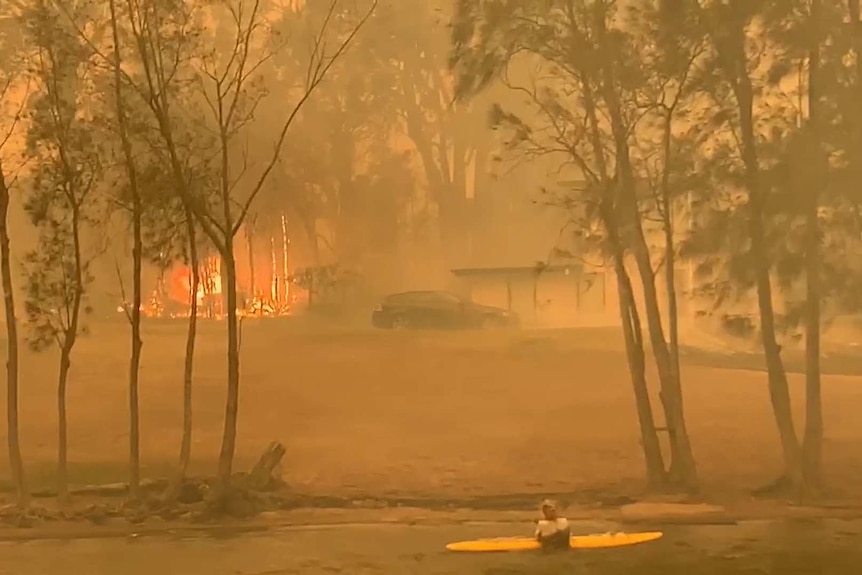 Fire burns on shore as a kayaker watches on.