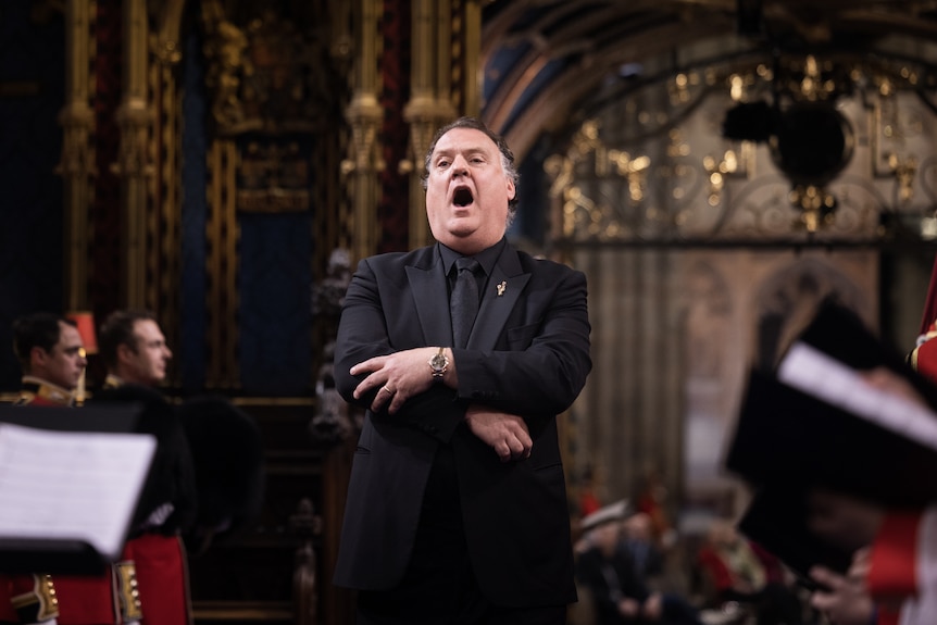 Sir Bryn Terfel in a black suit sings during King Charles Coronation in Westminster Abbey, with ornate architecture behind.